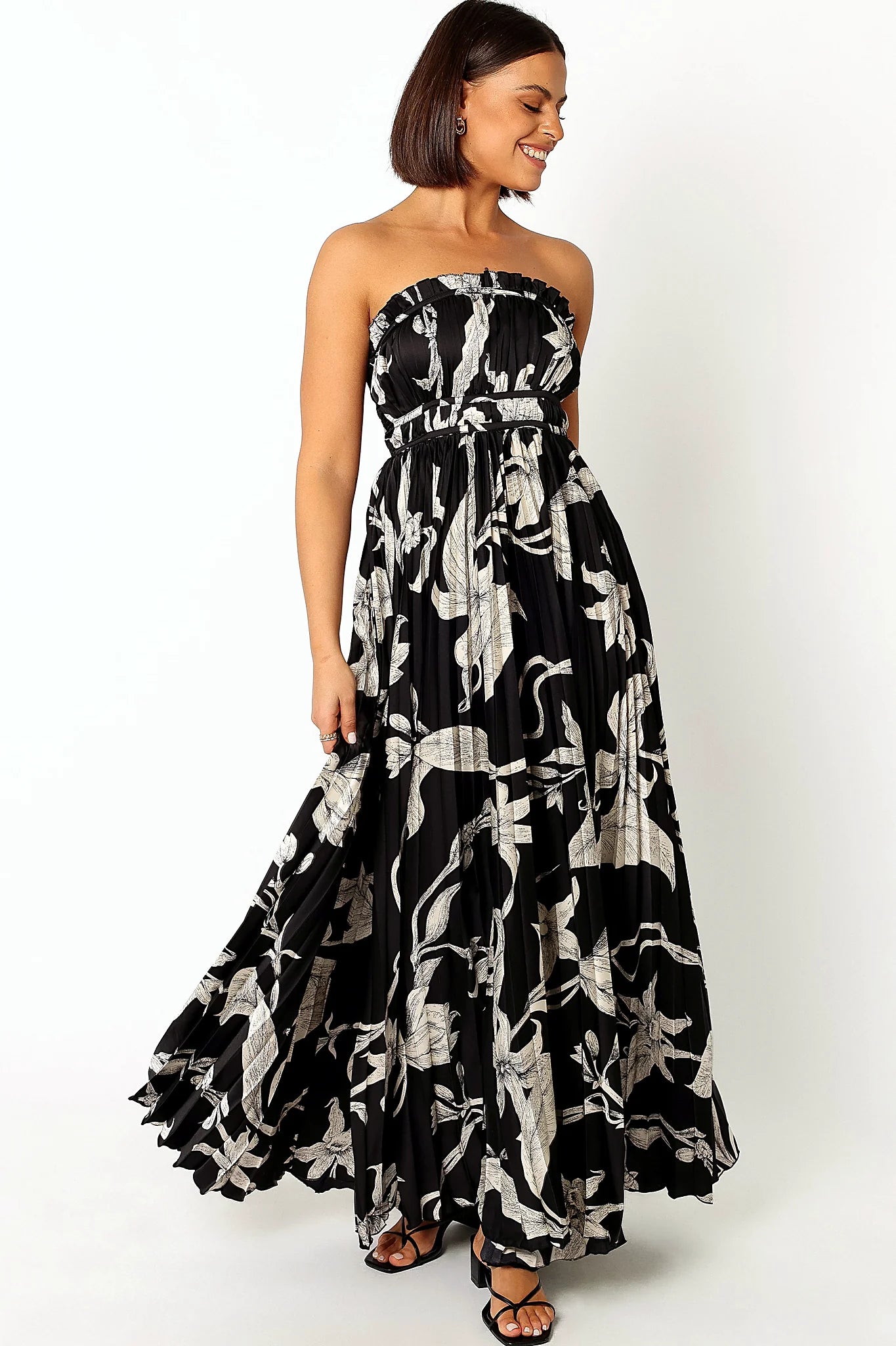 Front view of a strapless black floral maxi dress with fine pleats