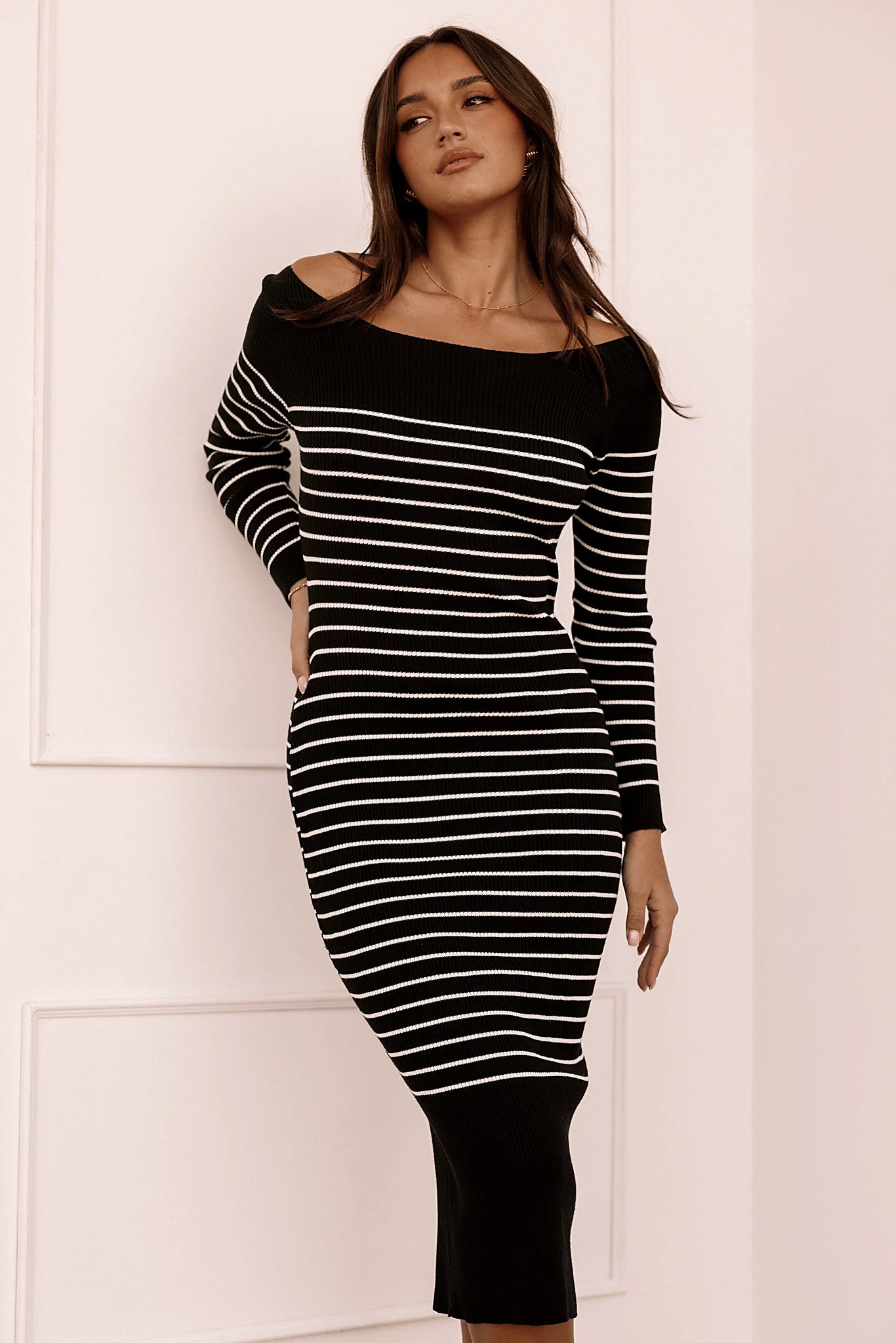 Front view of a black ribbed knit midi dress worn off the shoulder with long sleeves