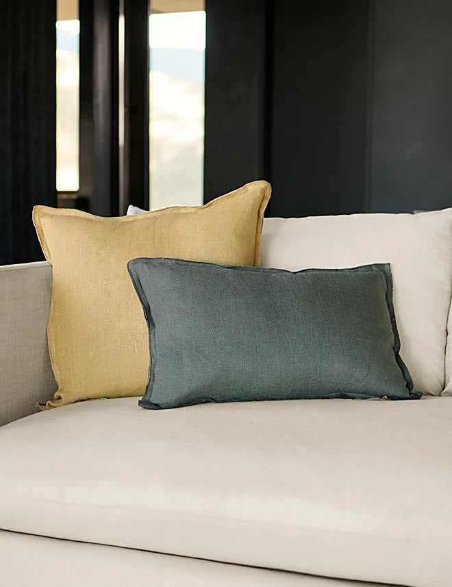 Linen lumbar pillow resting in front of larger cushions on a made bed