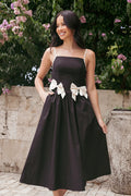 Front view of a black midi dress with white contrast trim and a waist bow